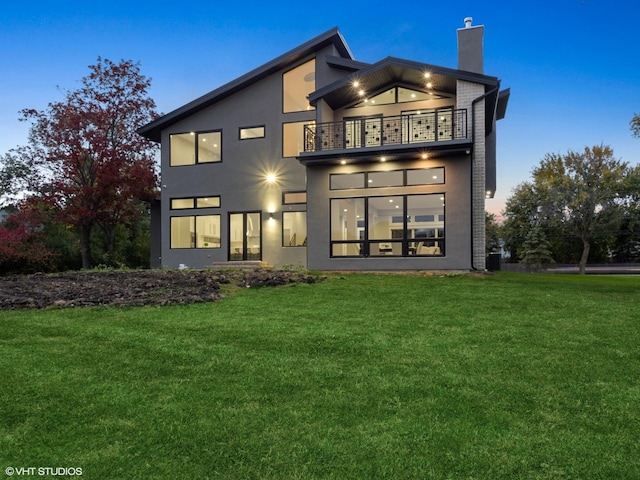 back house at dusk featuring a lawn, a balcony, and central air condition unit