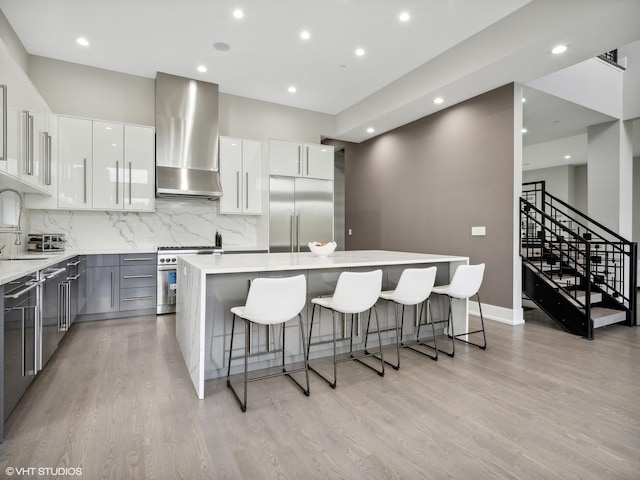 kitchen featuring a breakfast bar area, premium appliances, a kitchen island, wall chimney range hood, and white cabinets