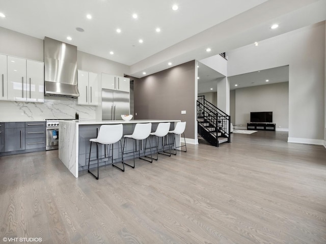 kitchen with a kitchen island, high quality appliances, white cabinets, a kitchen breakfast bar, and wall chimney exhaust hood