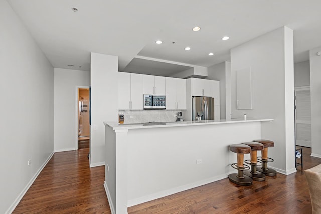 kitchen with appliances with stainless steel finishes, a breakfast bar area, white cabinets, kitchen peninsula, and dark wood-type flooring