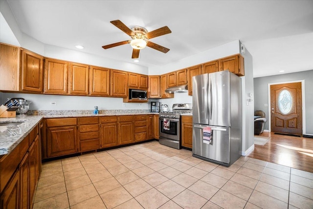 kitchen featuring light tile patterned flooring, sink, ceiling fan, stainless steel appliances, and light stone countertops