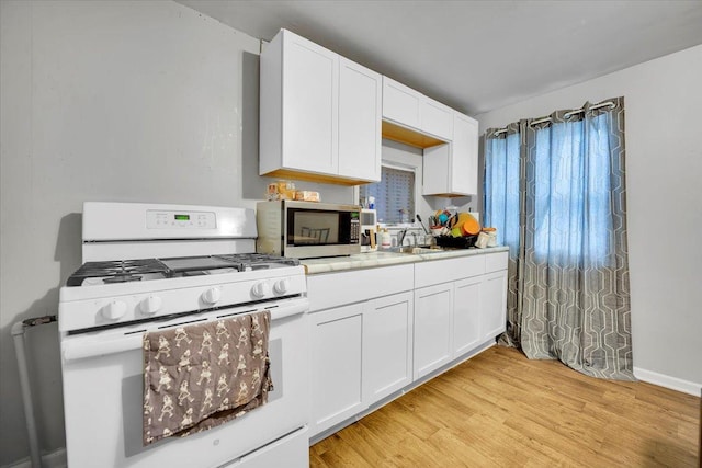 kitchen with sink, light hardwood / wood-style floors, white range with gas stovetop, and white cabinets