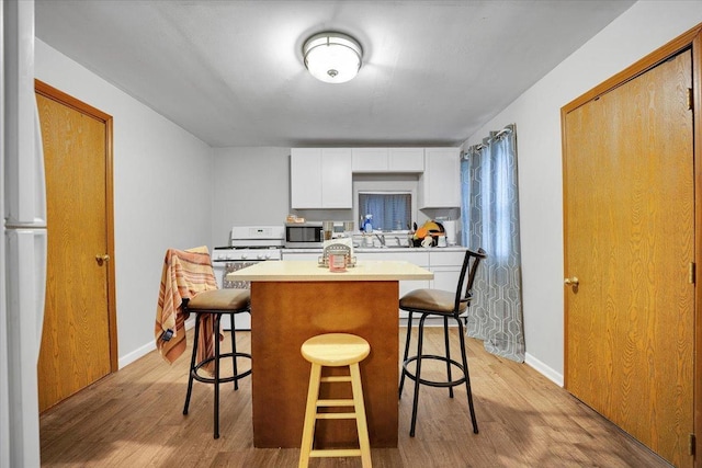 kitchen featuring white appliances, light hardwood / wood-style flooring, white cabinetry, a center island, and a kitchen bar