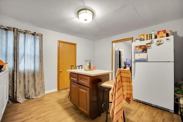 kitchen with a breakfast bar area, a kitchen island, white fridge, and light wood-type flooring