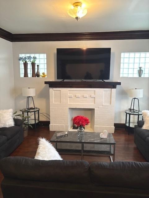 living room with dark wood-type flooring, ornamental molding, and a brick fireplace