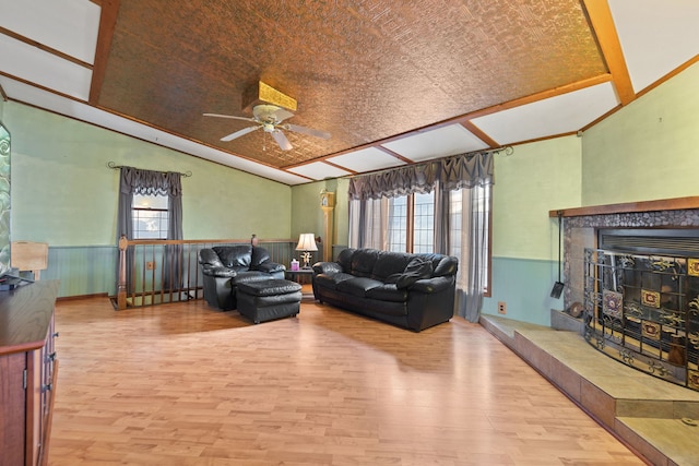 living area with a wainscoted wall, vaulted ceiling, a tiled fireplace, and wood finished floors