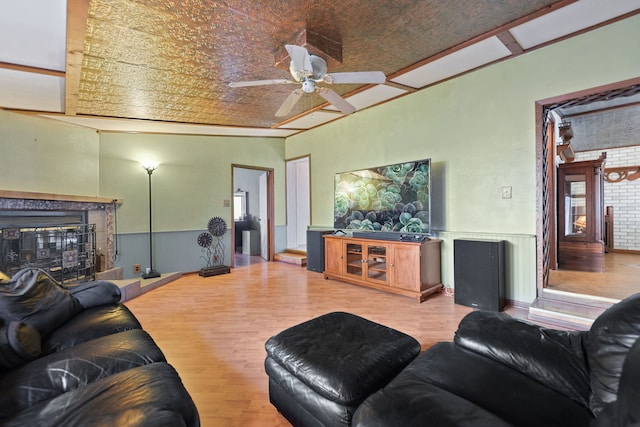 living area with a fireplace, a ceiling fan, wood finished floors, and wainscoting