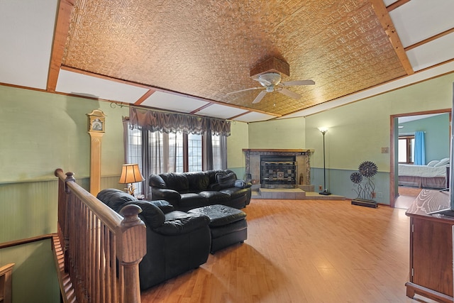 living area with a wainscoted wall, ceiling fan, a fireplace with raised hearth, and wood finished floors