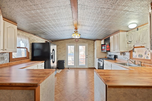 kitchen featuring black refrigerator with ice dispenser, a sink, wood counters, brick wall, and stainless steel gas range