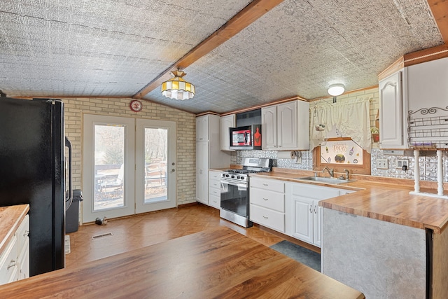 kitchen featuring lofted ceiling, brick wall, appliances with stainless steel finishes, wooden counters, and a sink