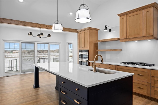 kitchen with sink, decorative light fixtures, appliances with stainless steel finishes, a kitchen island with sink, and light hardwood / wood-style floors