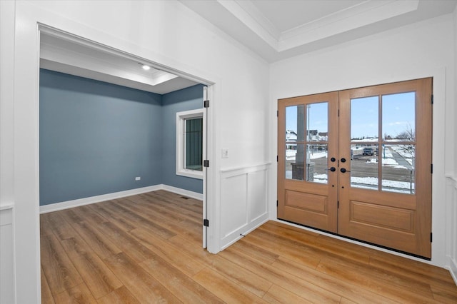 entryway featuring crown molding, a tray ceiling, french doors, and light wood-type flooring