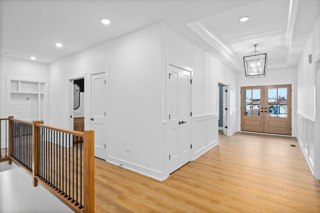 entrance foyer with a raised ceiling, a chandelier, light hardwood / wood-style floors, and french doors