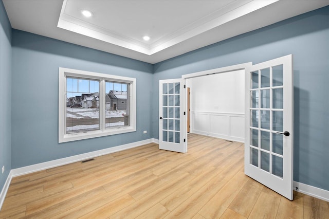 unfurnished room featuring a tray ceiling, ornamental molding, french doors, and light wood-type flooring