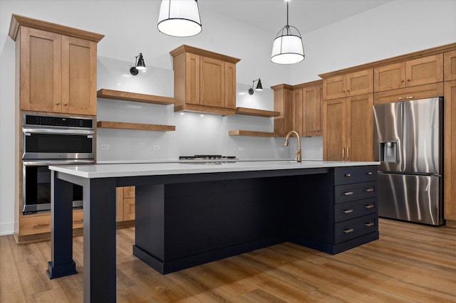 kitchen with pendant lighting, appliances with stainless steel finishes, an island with sink, and light wood-type flooring