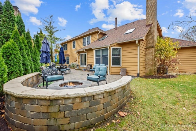 back of property with a fire pit, a patio area, and a lawn