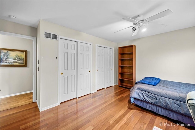 bedroom featuring multiple closets, wood-type flooring, and ceiling fan