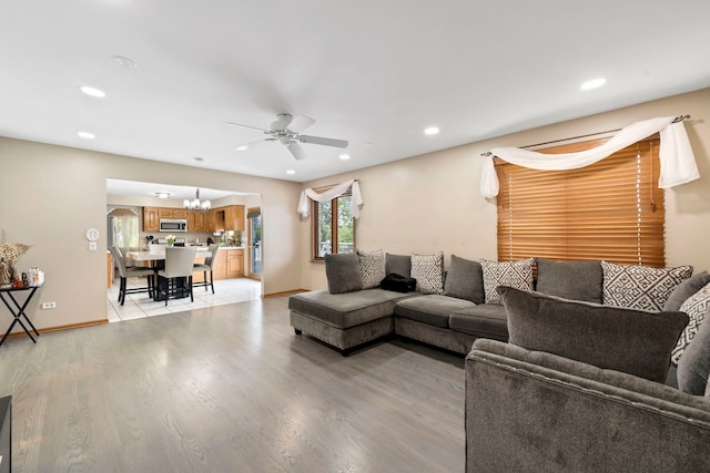 living room featuring ceiling fan with notable chandelier and light hardwood / wood-style flooring