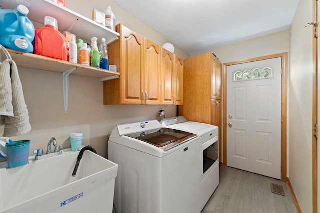 washroom featuring independent washer and dryer, cabinets, sink, and light hardwood / wood-style flooring