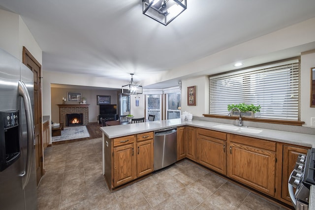 kitchen with pendant lighting, sink, stainless steel appliances, a fireplace, and kitchen peninsula