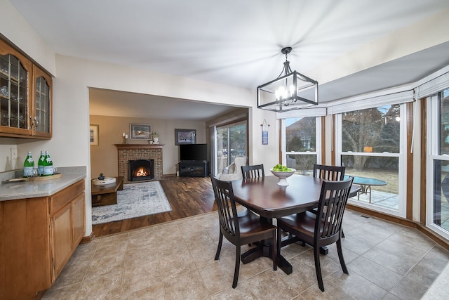 tiled dining space featuring a chandelier and a brick fireplace