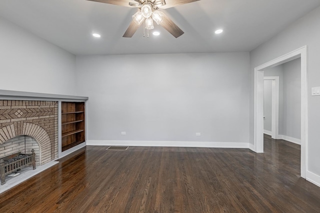 unfurnished living room with a brick fireplace, dark wood-type flooring, and ceiling fan