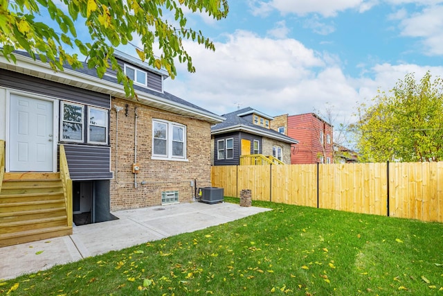 rear view of property featuring a yard, central AC unit, and a patio area