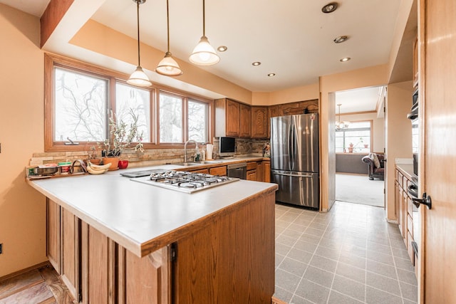 kitchen with brown cabinetry, a peninsula, stainless steel appliances, light countertops, and backsplash