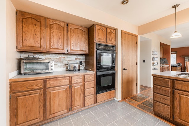 kitchen with dobule oven black, brown cabinetry, backsplash, and light countertops