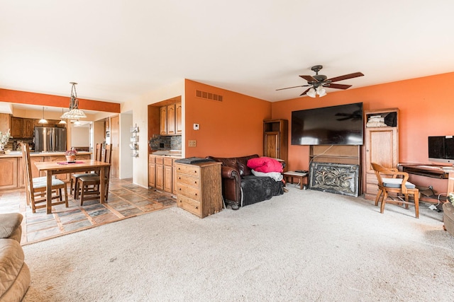 living room featuring a ceiling fan, visible vents, and light colored carpet