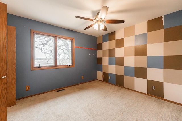 carpeted spare room with wallpapered walls, baseboards, visible vents, and a ceiling fan