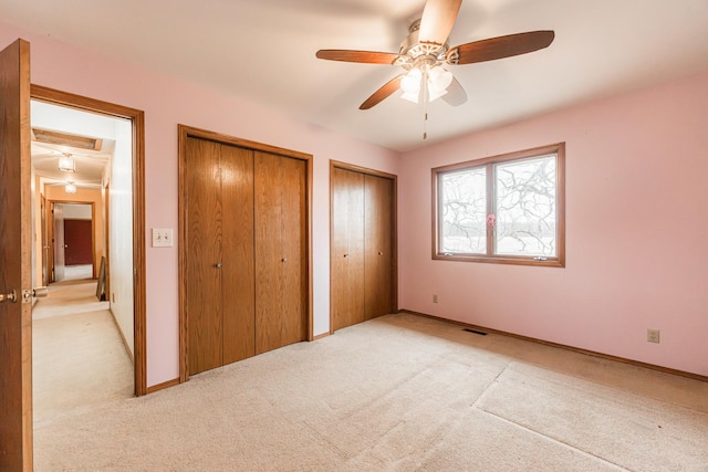 unfurnished bedroom featuring two closets, visible vents, light carpet, ceiling fan, and baseboards