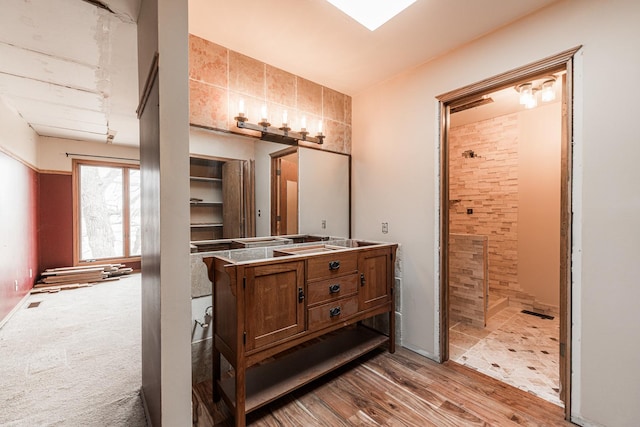 bathroom with double vanity, wood finished floors, and tiled shower