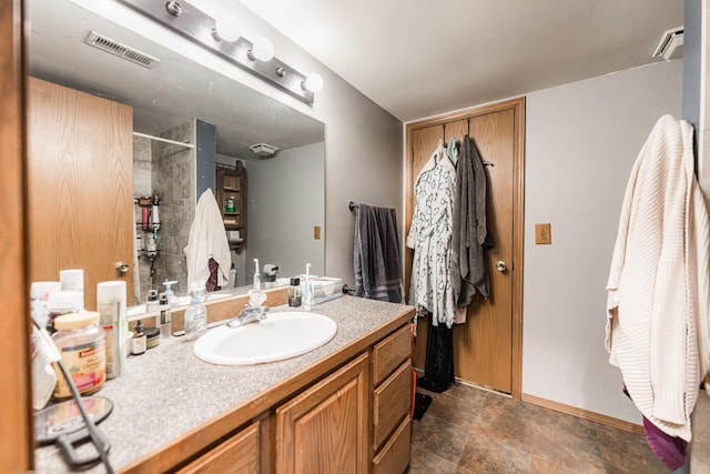 bathroom featuring visible vents, a tile shower, vanity, and baseboards