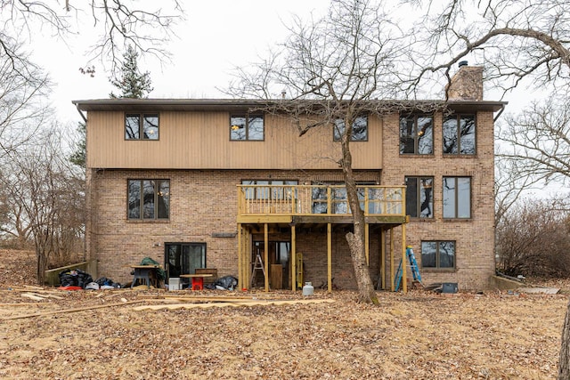 rear view of house featuring a deck, brick siding, and a chimney