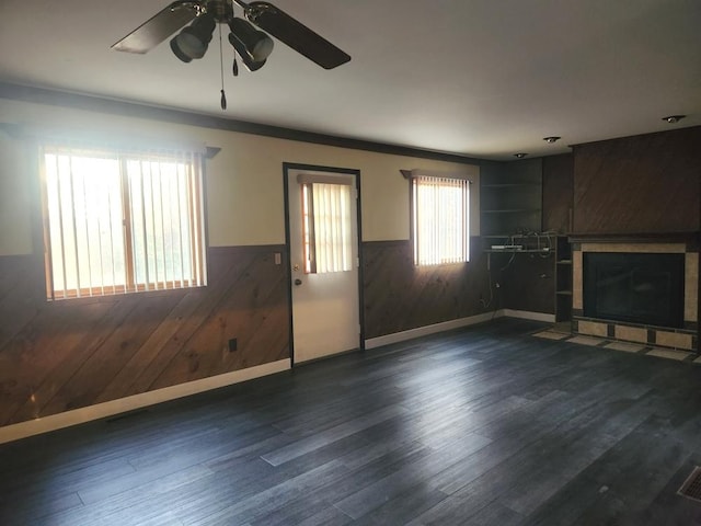 unfurnished living room with dark wood-type flooring, ceiling fan, a tiled fireplace, and wood walls