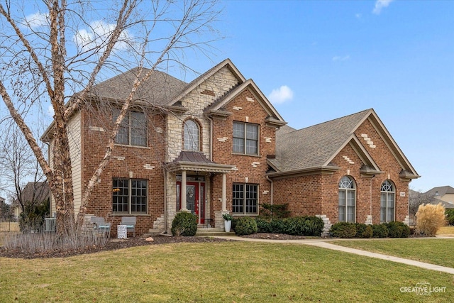 traditional-style house with stone siding, a shingled roof, a front lawn, and brick siding