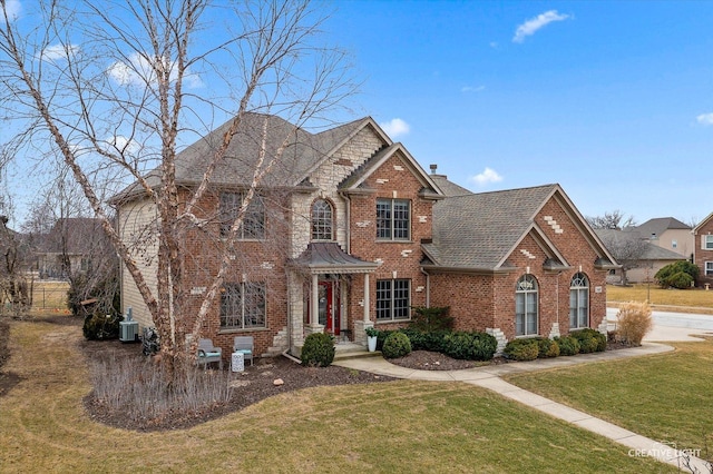 view of front facade with a shingled roof, a chimney, a front yard, central AC, and brick siding