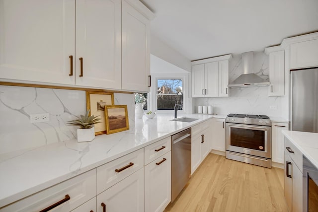 kitchen featuring wall chimney range hood, sink, appliances with stainless steel finishes, light stone counters, and white cabinets