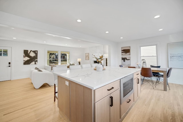 kitchen featuring stainless steel microwave, a wealth of natural light, light hardwood / wood-style floors, a kitchen island, and light brown cabinets