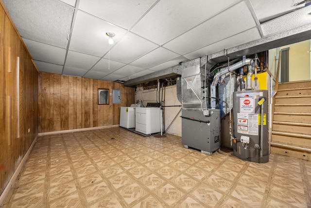 basement featuring a paneled ceiling, wood walls, water heater, separate washer and dryer, and electric panel