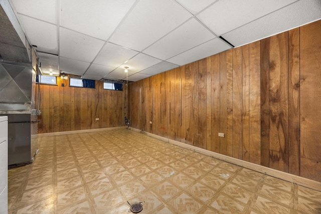 basement featuring a drop ceiling and wooden walls