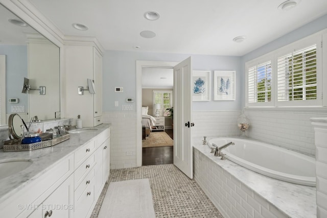 bathroom featuring tiled tub, vanity, a wealth of natural light, and tile walls