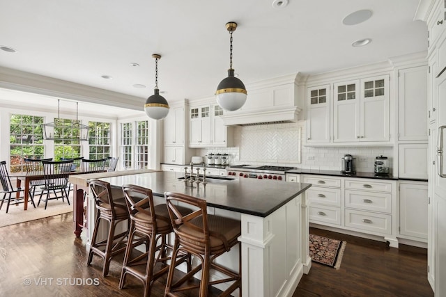 kitchen featuring sink, white cabinetry, a center island with sink, custom range hood, and pendant lighting