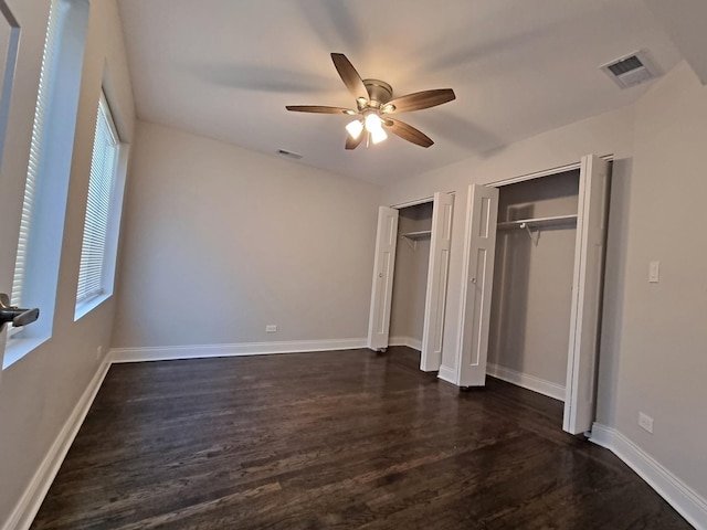 unfurnished bedroom featuring ceiling fan, dark hardwood / wood-style flooring, and two closets