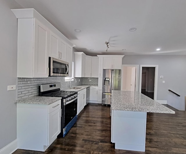 kitchen with sink, stainless steel appliances, light stone countertops, white cabinets, and a kitchen island