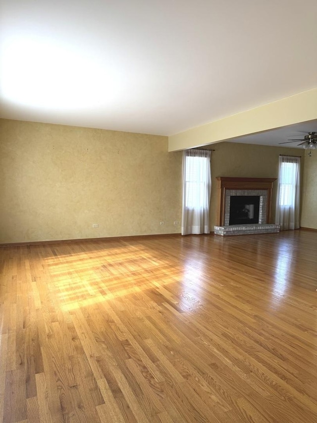 unfurnished living room with ceiling fan, a brick fireplace, light hardwood / wood-style flooring, and a wealth of natural light