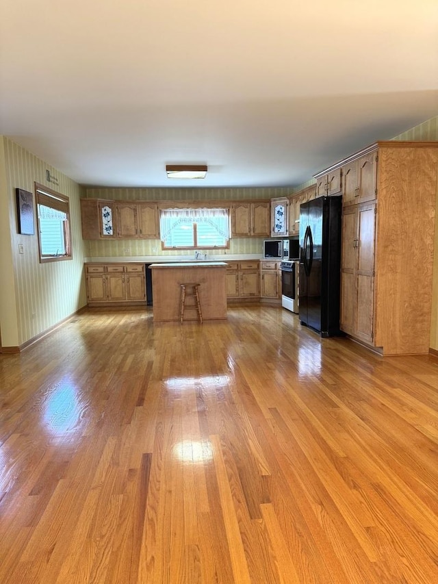 kitchen with electric stove, sink, light hardwood / wood-style flooring, stainless steel microwave, and black refrigerator with ice dispenser