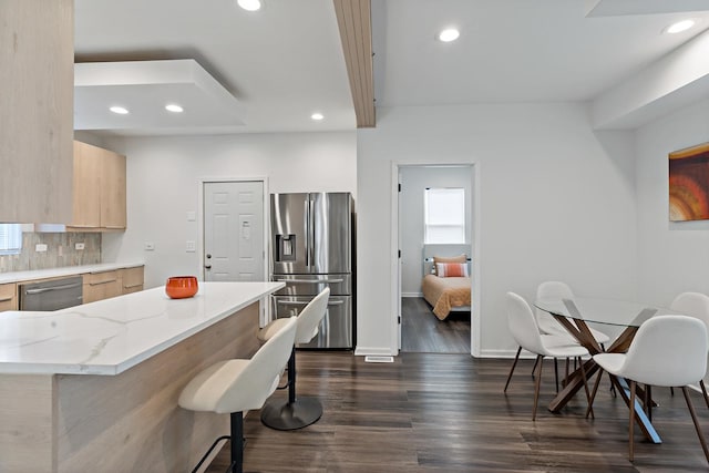 kitchen with dark wood-type flooring, appliances with stainless steel finishes, light stone countertops, a kitchen bar, and light brown cabinets