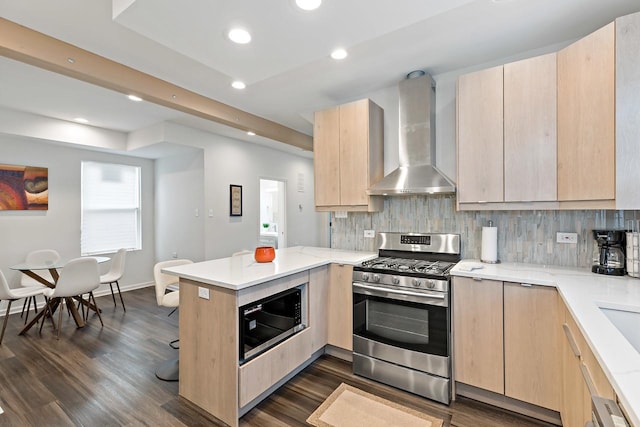 kitchen featuring light brown cabinetry, black microwave, kitchen peninsula, stainless steel gas range, and wall chimney exhaust hood